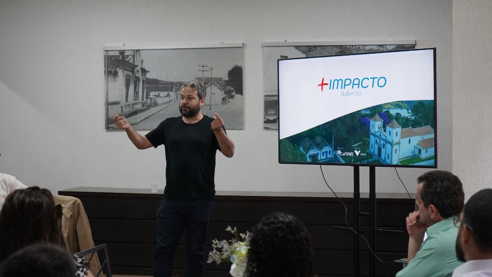 Thiago Alvim palestra ao lado de telão com a logo do projeto +Impacto